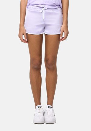 Personne portant un short violet clair à cordon et des baskets blanches, debout avec les bras détendus le long du corps sur un fond uni.