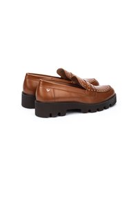 Mocasines de cuero marrón con una suela de goma estriada, que cuentan con una correa decorativa con tachuelas y un pequeño logo en el lateral.