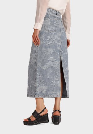Gonna maxy in denim con un intricato motivo bianco, spacco laterale, vita alta e due tasche posteriori. Abbinata a sandali con zeppa neri.