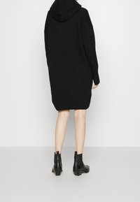 Abito felpa nero oversize con orli a costine, realizzato in un tessuto testurizzato. Abbinato a stivali neri alla caviglia con tacco basso.