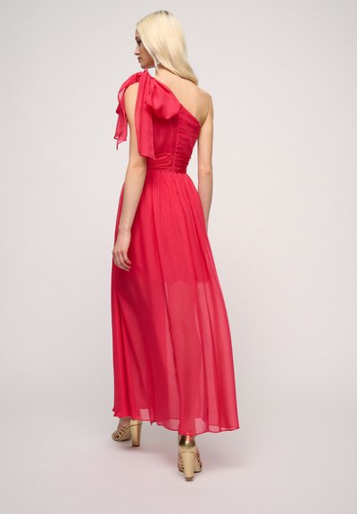 Long pink dress featuring a one-shoulder design, textured bodice, flowing skirt, and large bow detail on the shoulder. Smooth, airy fabric.