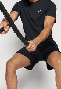 Svart träningströja och shorts med en vit Nike-logotyp. Tyget ser slätt och lätt ut, designat för aktiv prestation.