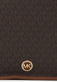 Brun monogramcanvas handväska med en guld MK-logotyp och en slät läderbotten. Texturerad yta med ett upprepande logomönster.