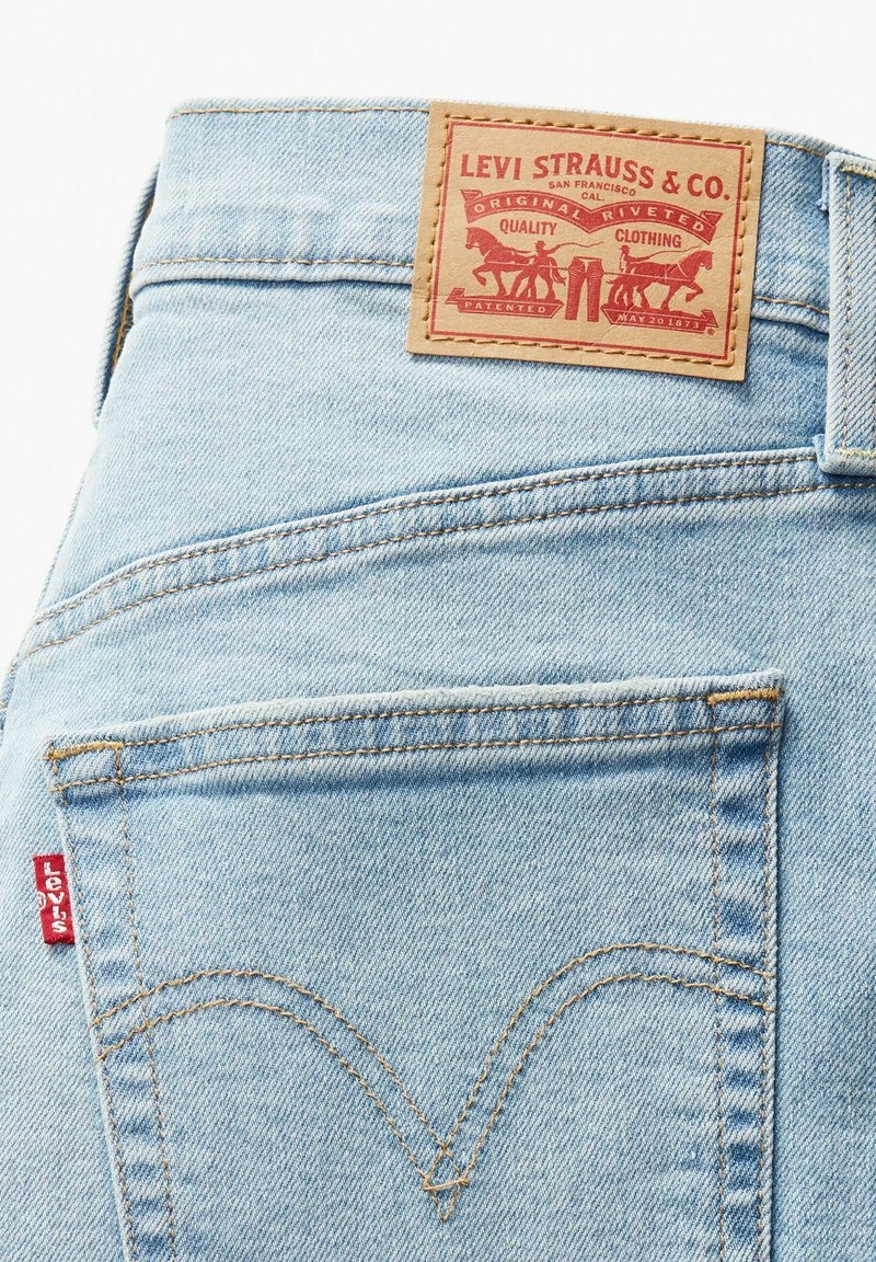Jeans de denim azul claro con un diseño clásico, un parche de cuero marrón en la cinturilla y una etiqueta roja de Levi's en el bolsillo trasero.