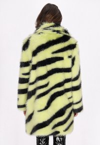 Cappotto in pelliccia sintetica con base verde lime e strisce nere a motivo tigre. Il design è oversize, con una texture morbida e colletto ampio.