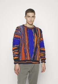 Strickpullover mit auffälligen Mustern in Blau, Orange und Schwarz, ergänzt durch strukturierte Designs. Der Rundhalsausschnitt und die gerippten Bündchen runden den Look ab.