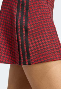 Red and black patterned skirt featuring a houndstooth design, with contrasting black side stripes and a smooth fabric texture.