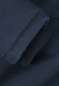 Țesătură albastră închisă cu o textură netedă, prevăzută cu un manșon tricotat cu nervuri; designul include o margine pliată și detalii subtile de cusătură.