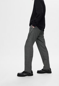 Gråmönstrade byxor med rak benpassform, kombinerade med en svart texturerad tröja och blanka svarta loafers.