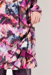Abito a maniche lunghe con un motivo astratto colorato nei toni del rosa, viola e blu. Presenta polsini elasticizzati e un orlo arricciato.