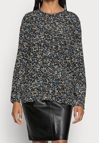Langärmliges Shirt aus dunklem Stoff mit einem bunten, gesprenkelten Muster in Blau, Orange und Weiß, kombiniert mit einem schwarzen Lederrock.