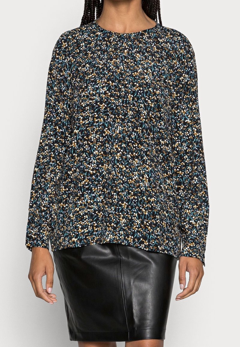 Langärmliges Shirt aus dunklem Stoff mit einem bunten, gesprenkelten Muster in Blau, Orange und Weiß, kombiniert mit einem schwarzen Lederrock.