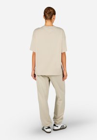 Bēšas krāsas pārspīlēts T-krekls, brīvs piegriezums, īsas piedurknes, apvienots ar atbilstošām bēšas krāsas sporta biksēm un baltām sporta apavām ar melnām svītrām.