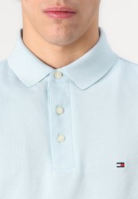 Polo di colore blu chiaro realizzato in un tessuto texturizzato, dotato di un colletto classico, tre bottoni e un piccolo logo ricamato sul petto.