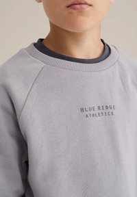 Felpa grigia chiara con maniche raglan, colletto a coste e "BLUE RIDGE ATHLETICS" ricamato in grigio scuro sul davanti. Texture liscia.