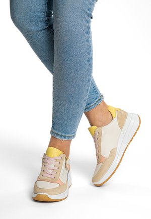Sporty sneakers featuring a mix of white leather, beige suede, and pink accents, with a textured sole and yellow heel detail.