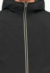 Black hooded jacket featuring a central zipper with a white accent. Made of smooth fabric with a lightweight, matte texture.