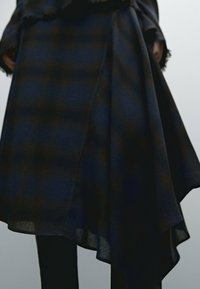 Jupe en plaid bleu marine à ourlet asymétrique, fabriquée dans un tissu doux et texturé. Elle présente des bords frangés et une silhouette drapée.