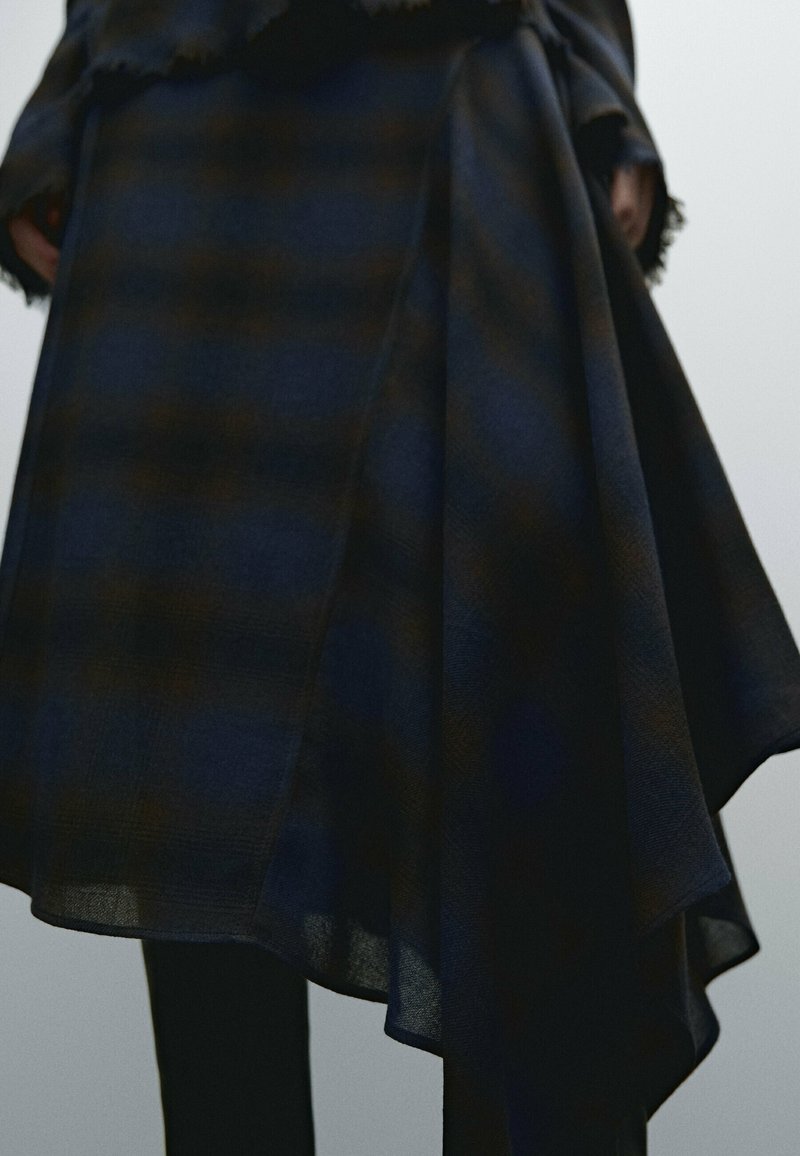 Jupe en plaid bleu marine à ourlet asymétrique, fabriquée dans un tissu doux et texturé. Elle présente des bords frangés et une silhouette drapée.