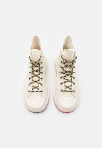 High-top sneakers made of cream canvas with multicolored speckles. Features colorful laces and solid rubber soles, purple and red accents.