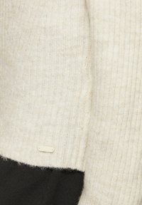 Crème kleurige geribbelde gebreide trui met een zwarte zoom en een klein wit label met het "QS" logo. Zachte textuur met een getailleerd ontwerp.
