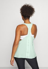 Jasno miętowy top na ramiączkach z designem typu racerback, z teksturowanym tyłem i warstwowym detalem materiału. W połączeniu z czarnymi legginsami.
