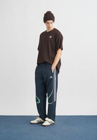 Ruda trumpomis rankovėmis marškinėliai su balta logo, derinami su tamsiai mėlynais sportinėmis kelnėmis su žaliais akcentais ir baltais šoninės juostos. Balti sportbačiai.