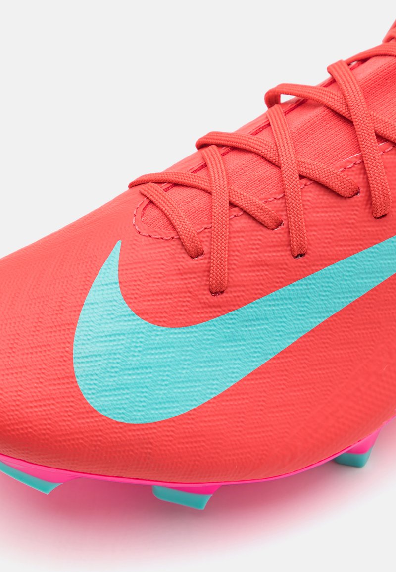 Scarpa da calcio corallo brillante con superficie texturizzata, logo Nike turchese e suola rosa. Presenta un sistema di allacciatura standard per una vestibilità sicura.