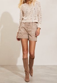 Ljusbeige stickad tröja med geometriska mönster, matchad med tanfärgade shorts med framfickor. Modellen bär tanfärgade mockastövlar som går upp till knäna.