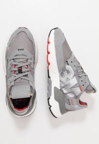 Šedé sportovní tenisky z materiálů mesh a semiš, s vzorovaným designem, červenými akcenty a bílou, polstrovanou podešví.