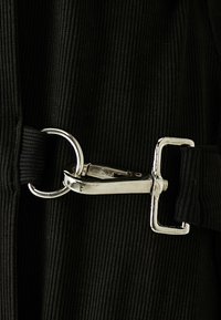 Czarna tkanina sztruksowa z metalowym, srebrnym zapięciem i klamerką. Tekstura jest żebrowana, z okrągłym pierścieniem D przymocowanym.
