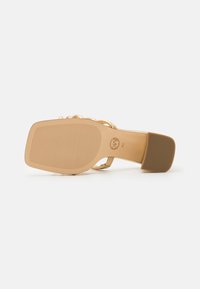 Hælhøye sandaler med en brune teksturert såle, gull metalliske stropper og lukket bak. Har flat tå og et mønstrede grep.
