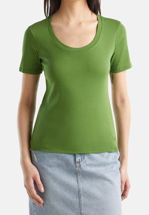 Kobieta ubrana w dopasowany zielony t-shirt z krótkim rękawem i okrągłym dekoltem oraz jasnoniebieską jeansową spódnicę z wysokim stanem.