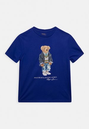 Navyblå t-shirt med en bjørn iført en stribet blazer, sweater, slips, revnede jeans og sneakers med teksten Polo Bear by Ralph Lauren nedenunder.