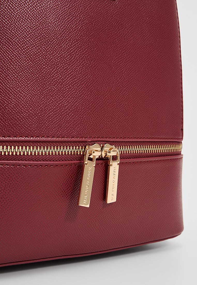Borsa in ecopelle testurizzata bordeaux con zip dorata. Presenta doppi cursori della zip con marchio inciso e una silhouette strutturata.