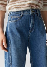 Jean en denim bleu clair coupe droite, taille haute, conception à cinq poches, surpiqûres contrastantes et texture subtile.