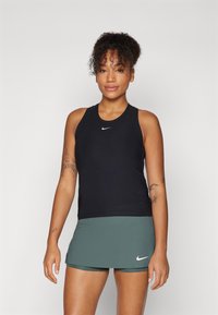Black Nike tank top with a round neckline, featuring a white logo on the chest, paired with an olive green skirt with shorts underneath.