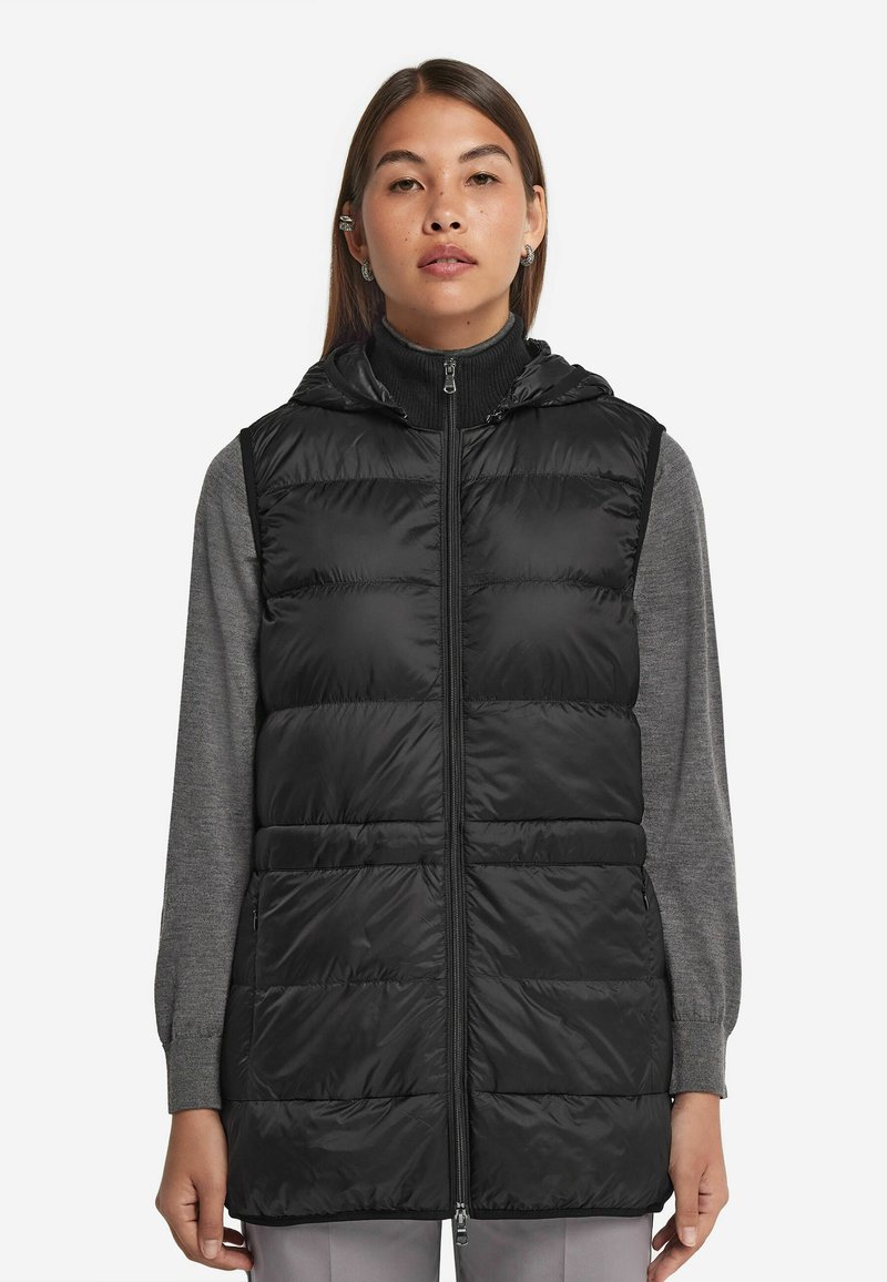 Czarna kamizelka puchowa z kapturem, z pikowanym wzorem, zamkiem z przodu i kieszeniami po bokach, noszona na szarym longsleeve.