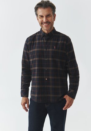 Donkergebloemde shirt met blauwe, rode en gele lijnen, met een button-down kraag, lange mouwen en een klein logo op de linkerkant van de borst. Draagt het met donkere spijkerbroek.