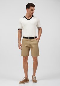 Polo de punto de manga corta en crema con detalles en negro, combinado con pantalones cortos beige y zapatillas marrones con cordones blancos. Diseño simple y clásico.