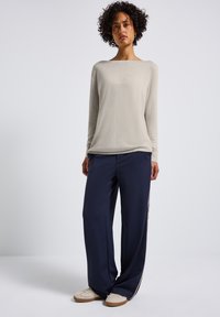 Lichtbeige lange mouw top met een bootnek, gecombineerd met donkerblauwe wijde broek met een zijstreep en textuur crème schoenen.