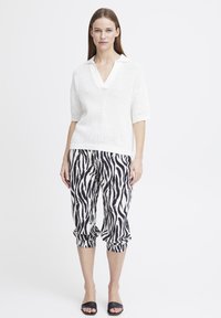Maglione bianco a maglia con maniche corte e scollo a V, abbinato a pantaloni tapered a strisce zebra bianco e nero e sandali neri a scivolo.