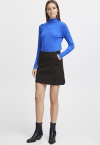 Modra dolgonamizasta majica s turtleneck izrezom, v kombinaciji s črno mini krilom, ki ima žepe. Nosi se z črnimi gležnjarji z božnimi zadrgami.