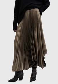 Plissé maxi rok in een gedempte olijfgroene kleur, met een gestructureerde stof en een asymmetrische zoom, gecombineerd met zwarte haklaarzen.