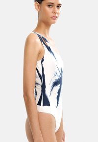 Jednoczęściowy strój kąpielowy w off-white z granatowym wzorem palm, z okrągłym dekoltem i cienkimi ramiączkami dla smukłej sylwetki.