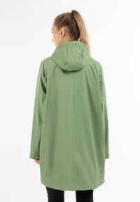 Grön vattentät regnrock med huva; slät, matt textur; knälång design; minimala söms detaljer; figursydda långärmar.
