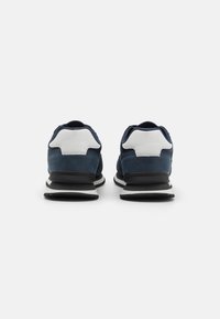 Navy and white athletic shoes with a suede upper, contrasting heel detail, and black and white striped sole. Rounded toe design.