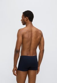 Μπλε ναυτικό μαγιό με εφαρμοστή σχεδίαση, λεία υφή και μαλακή μέση, εμφανιζόμενο από πίσω σε μοντέλο.