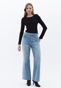 Svart långärmad topp med blommiga detaljer på axlarna, tillsammans med ljusblå vida jeans och svarta klackade ankelstövlar.