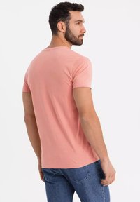 Maglietta a maniche corte in cotone rosa con scollatura rotonda, texture liscia e design aderente, abbinata a jeans in denim blu.